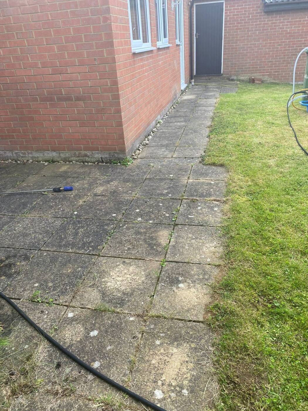 Grimy concrete paving slabs along house side path before cleaning