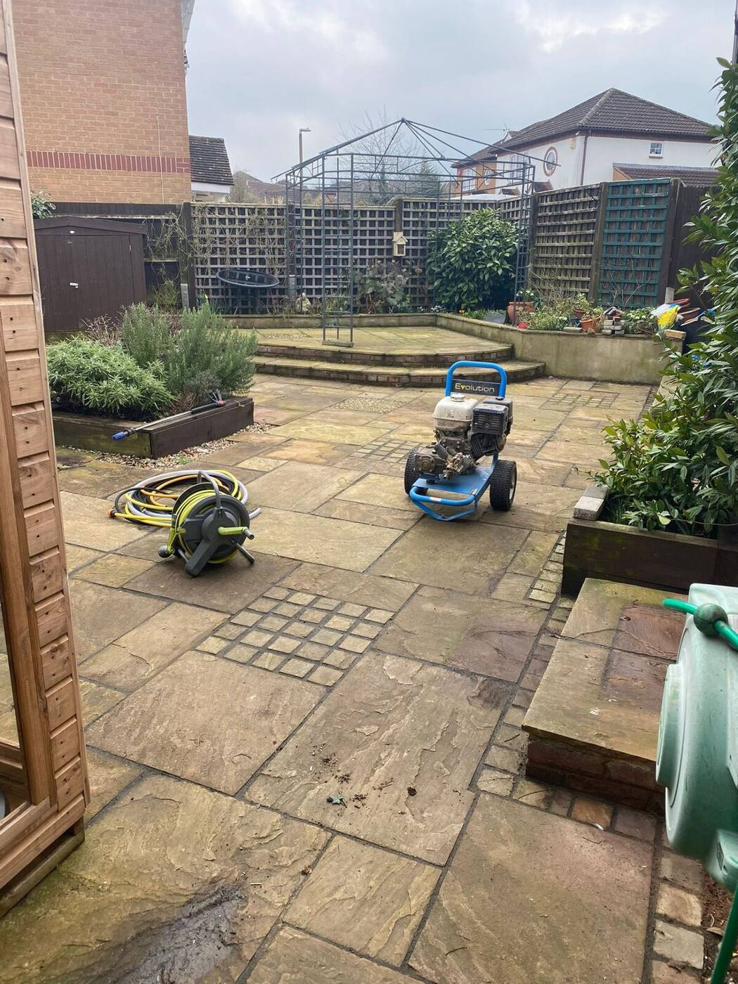 Algae-covered natural stone patio with pressure washer equipment ready for cleaning